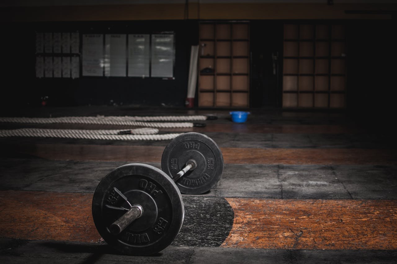 about-01 A lone barbell rests in an empty, dimly lit gym, emphasizing strength and solitude.