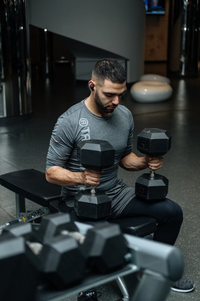 our-services-3 Adult man lifting dumbbells in a gym, focused on strength training workout.